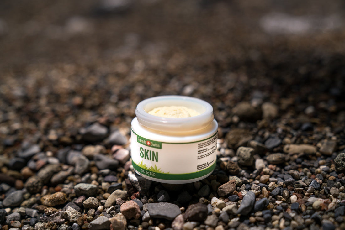 Åben krukke med Formula Swiss CBD Skin-salve, 300 mg CBD, på en stenstrand