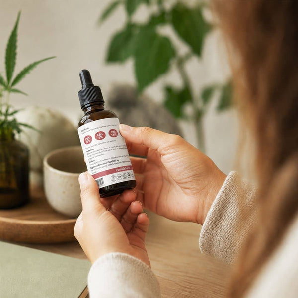 Kvinde læser etiketten på et Formula Swiss cannabinoidolieprodukt i naturlige indendørs omgivelser.