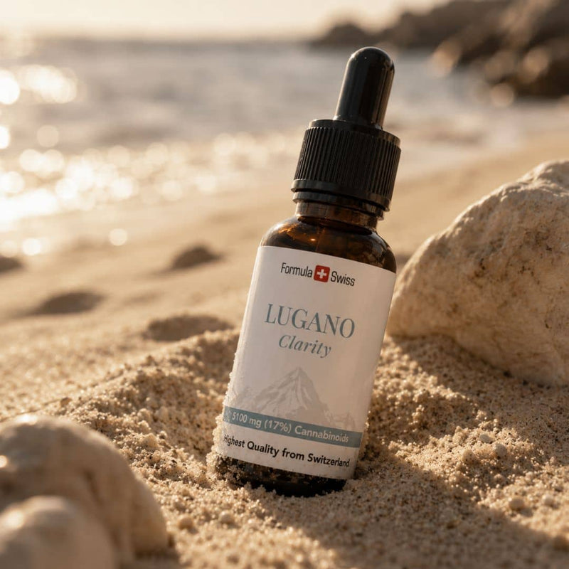 Formula Swiss Lugano Clarity CBD olieflaske placeret i strandsand ved siden af sten og solbelyst vand.